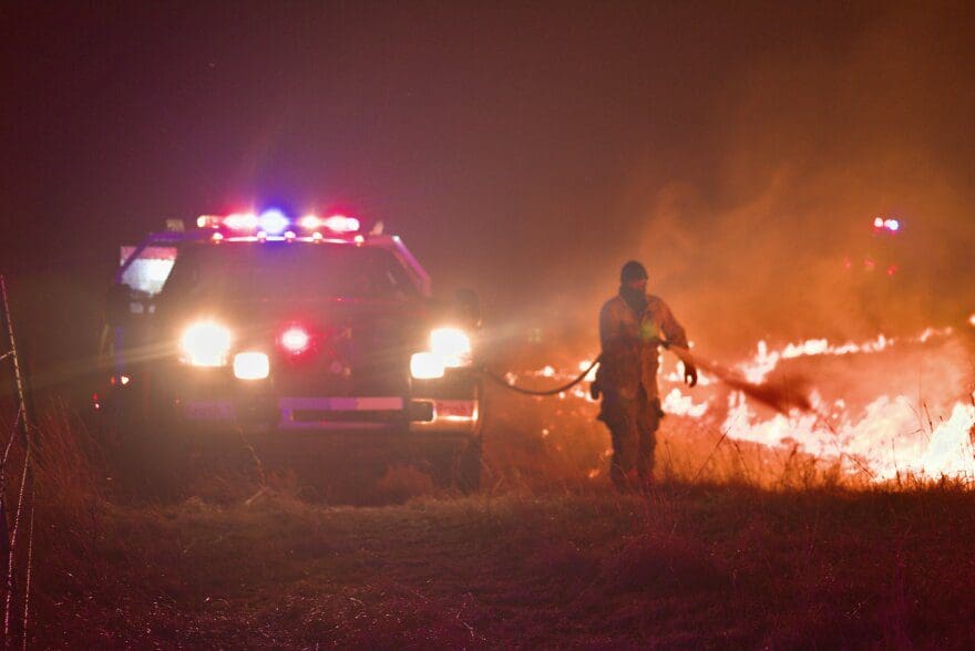 A firefighter sprays water onto a grassfire at night