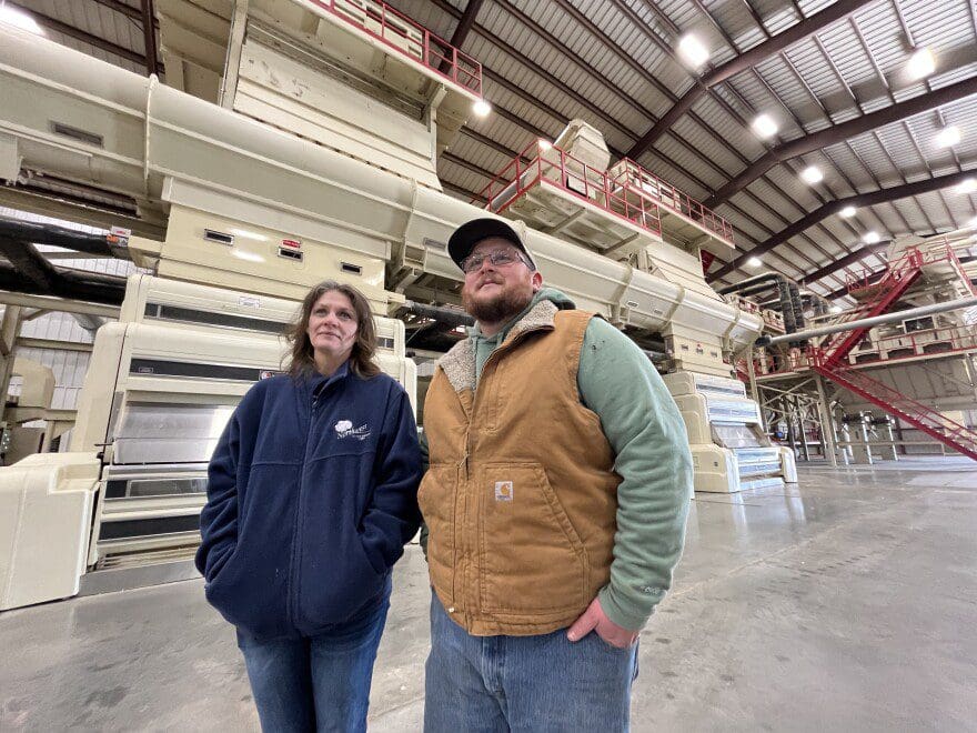 A man and woman stand in front of cotton ginning machinery