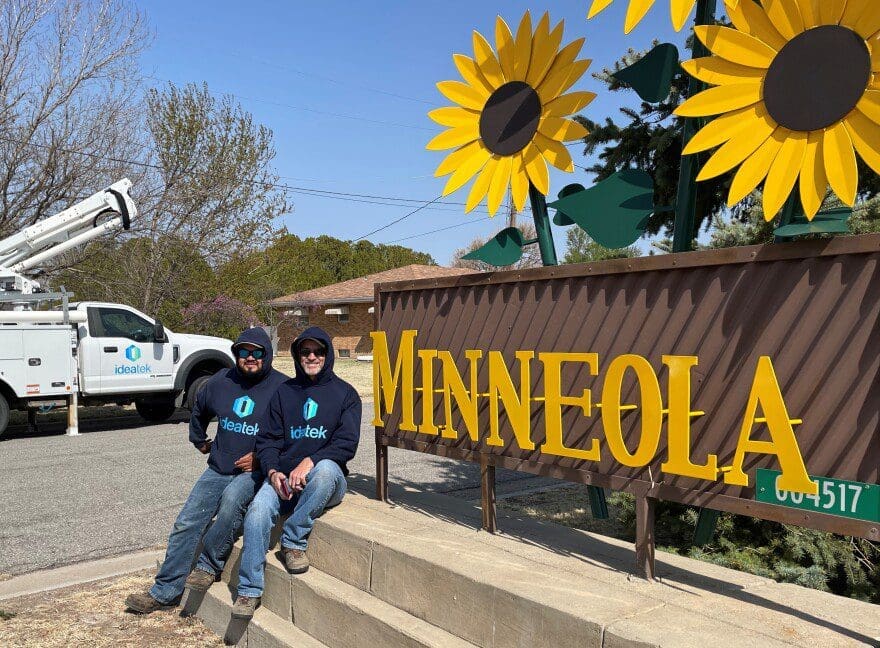 Two men sitting next to a sign that says Minneola