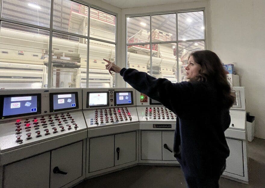 A woman points to part of a cotton gin operation